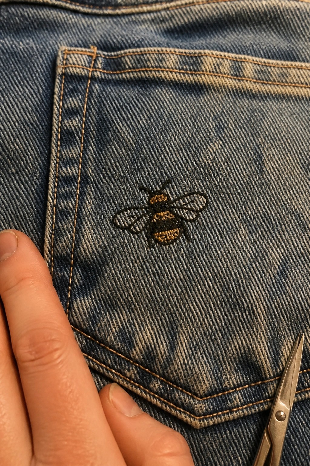 Bee embroidered in black and yellow thread on the back pocket of blue denim jeans.
