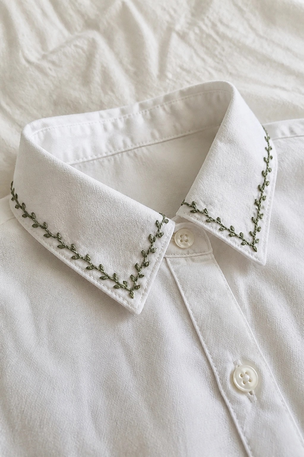 White shirt collar with delicate green leaf embroidery and white buttons.