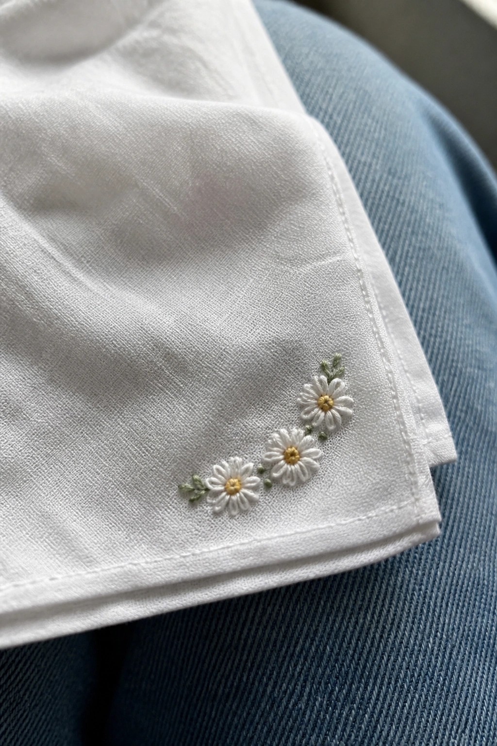 White fabric with daisy embroidery resting on blue denim jeans