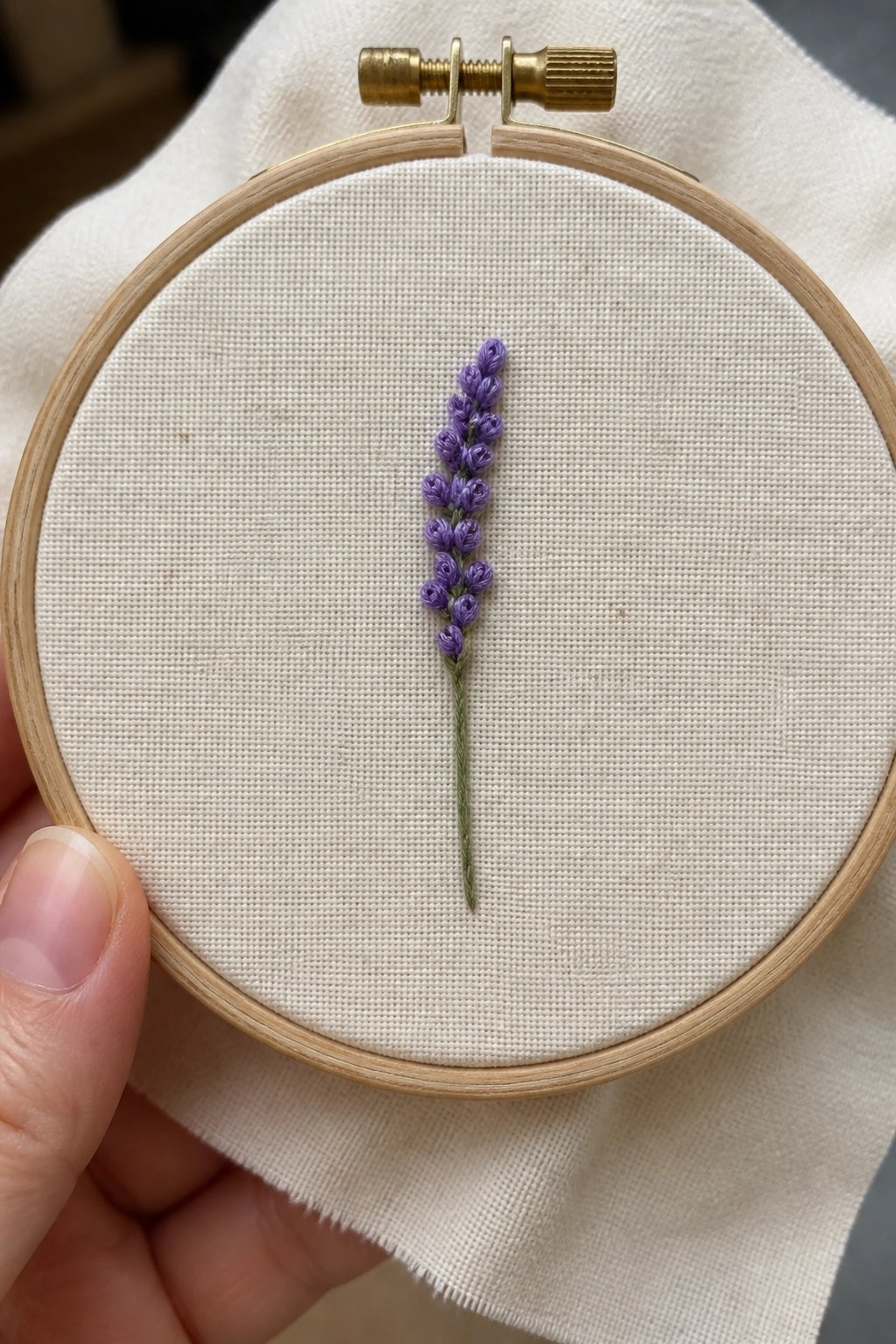 Hand holding wooden hoop with purple lavender embroidery on white fabric