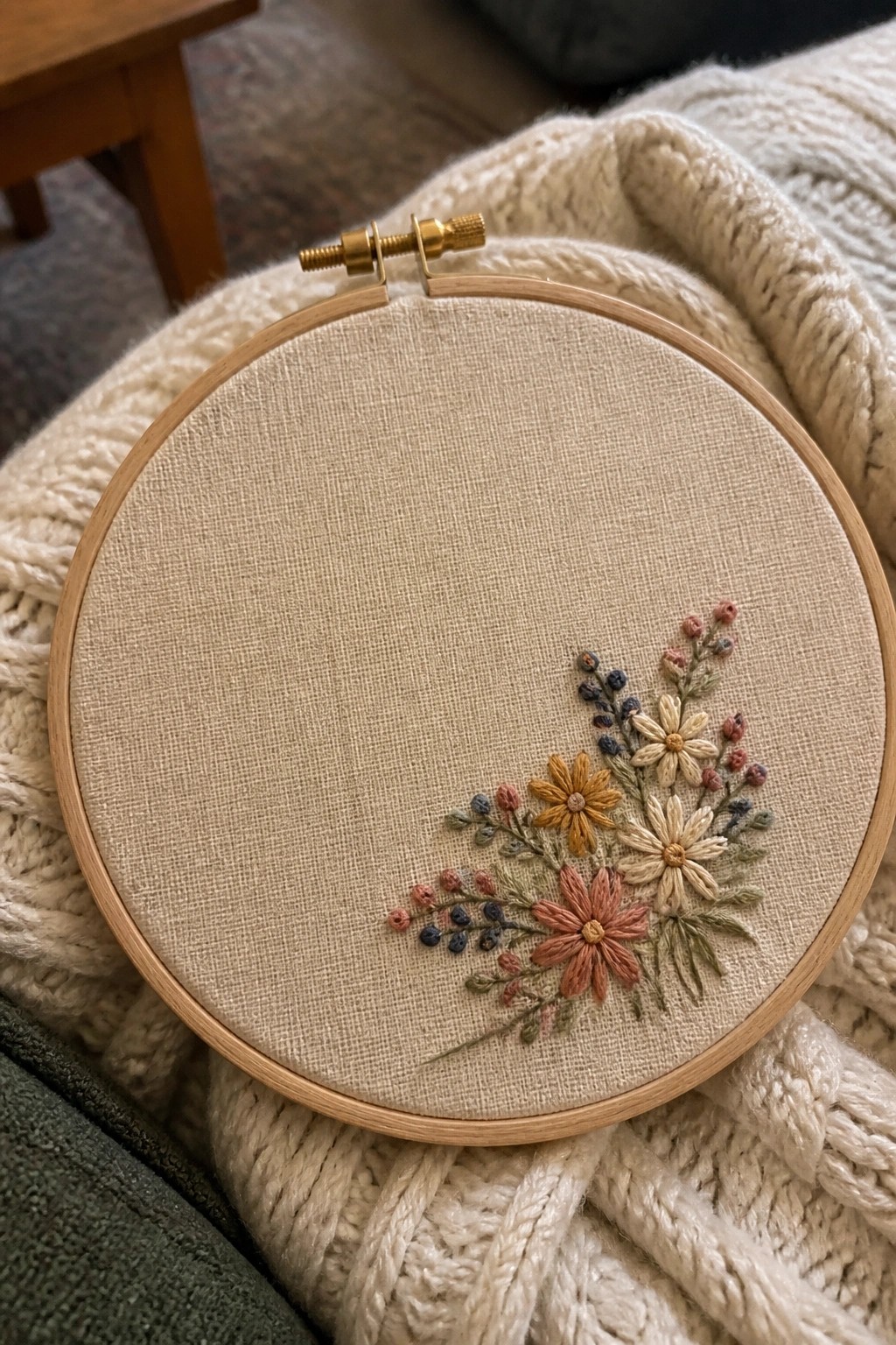 Wooden hoop with pink yellow floral embroidery on beige fabric over white knit blanket