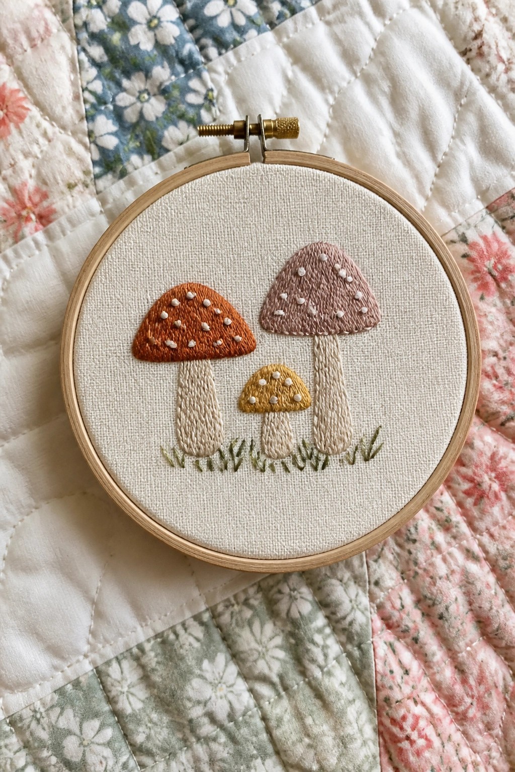 Three embroidered mushrooms in an embroidery hoop on floral quilt fabric.