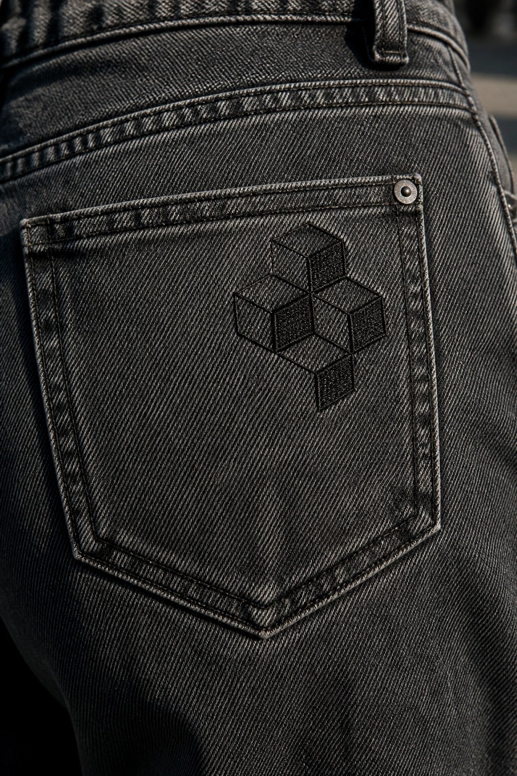 Dark denim back pocket with embroidered geometric cube logo and metal rivet