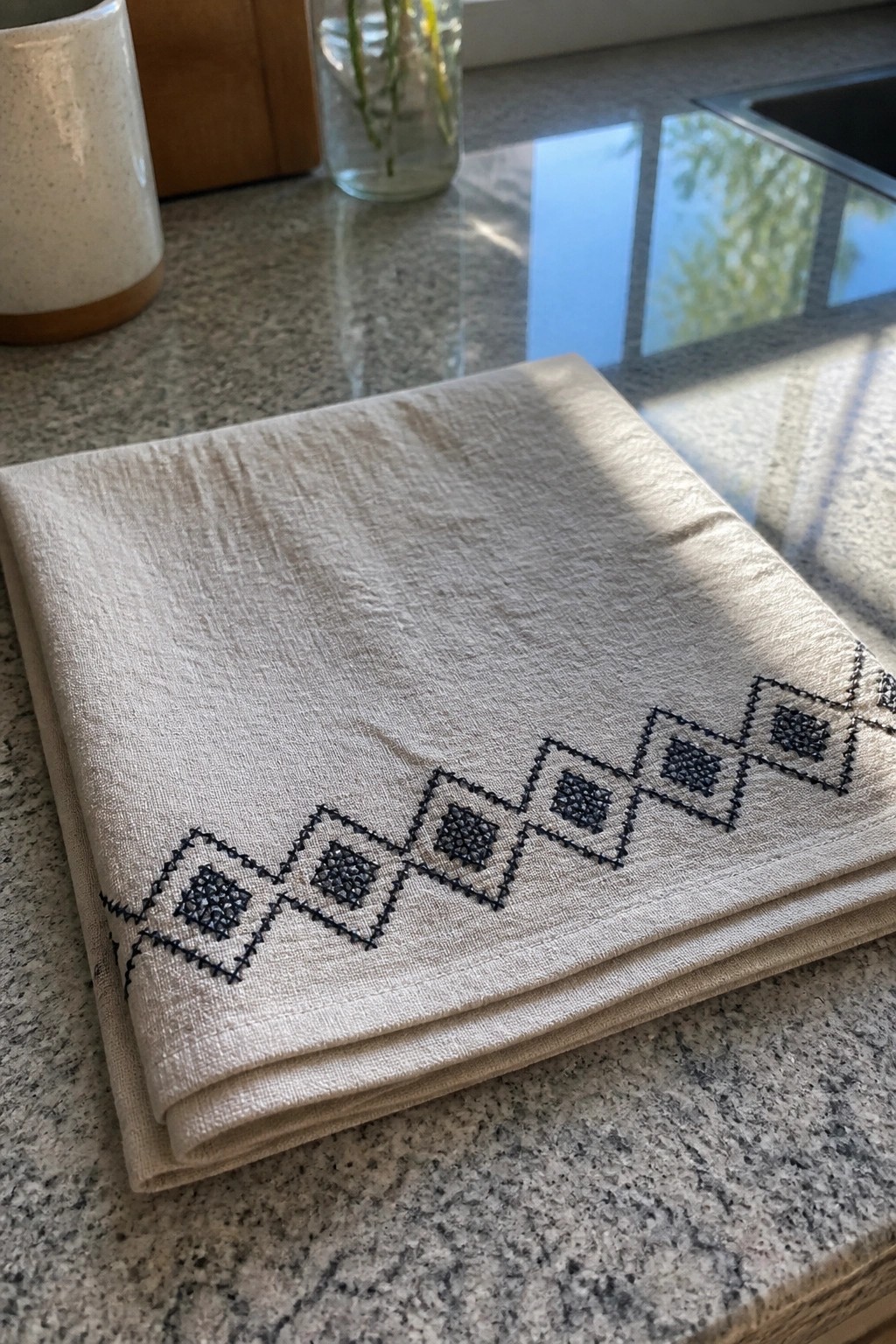 Folded off-white fabric with a black geometric border of diamonds and squares embroidered along one edge.