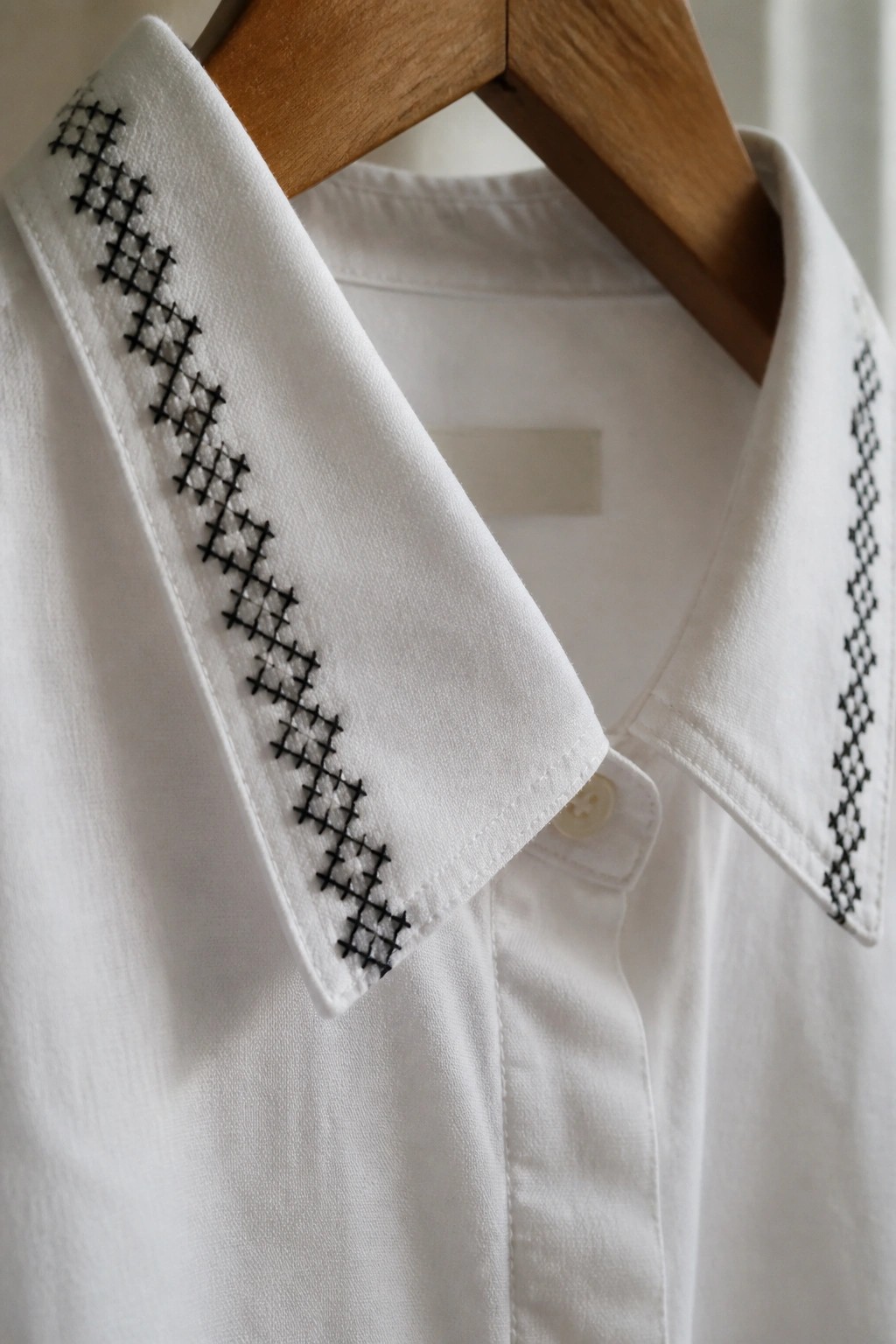 White shirt collar with black geometric lattice embroidery along both edges.