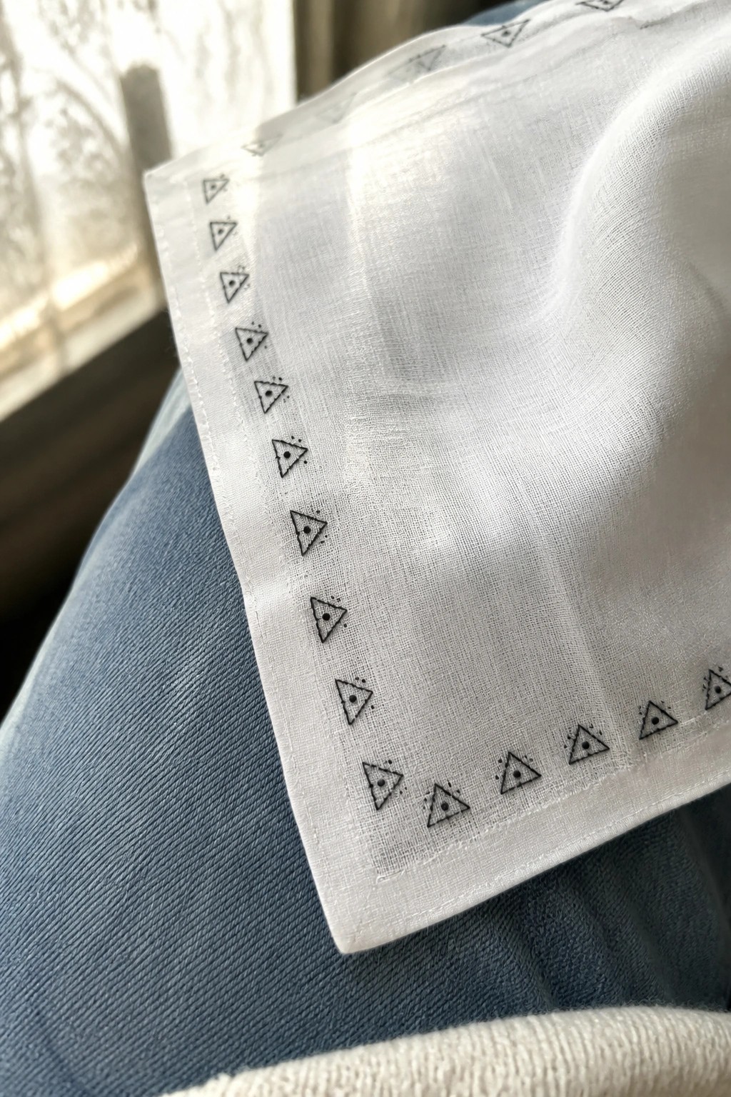 White handkerchief with black triangle patterns draped over blue denim jeans.