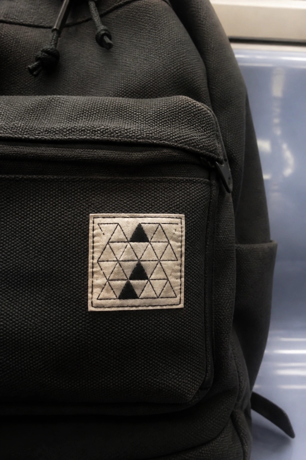 Black backpack with square beige patch of black geometric triangles on front pocket.