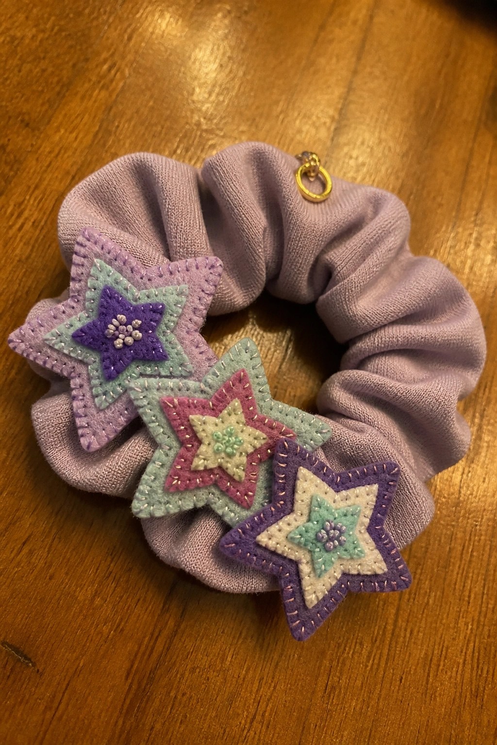 Lavender scrunchie with layered pastel felt stars and gold charm on wood