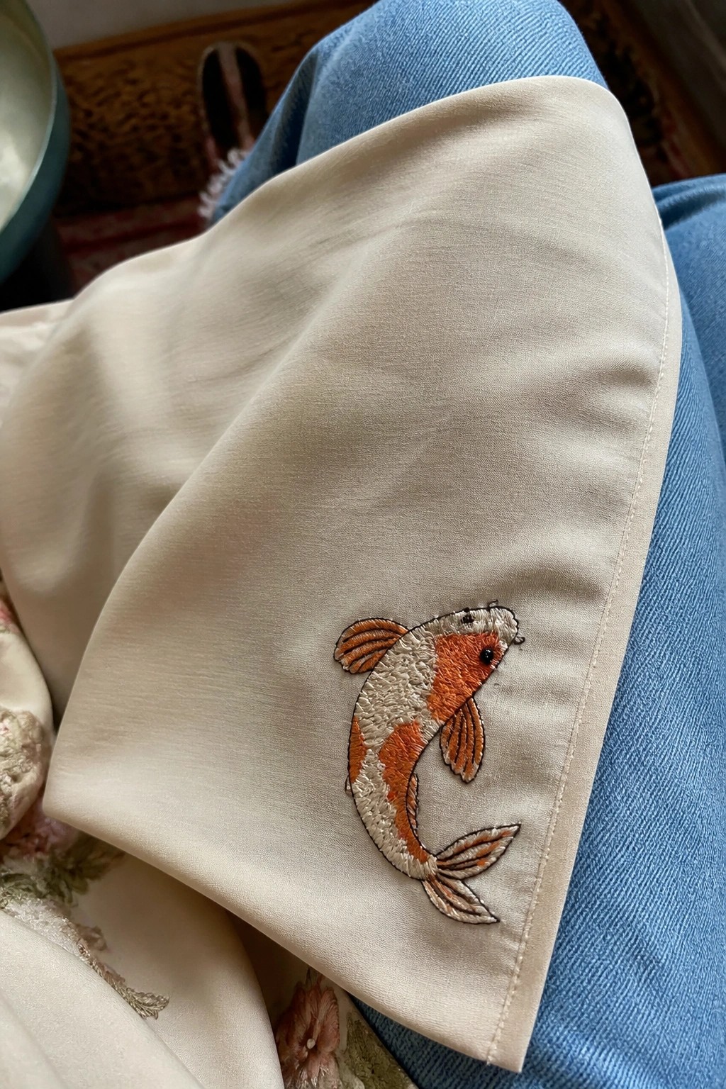 Orange and white koi fish embroidered on cream fabric over blue jeans