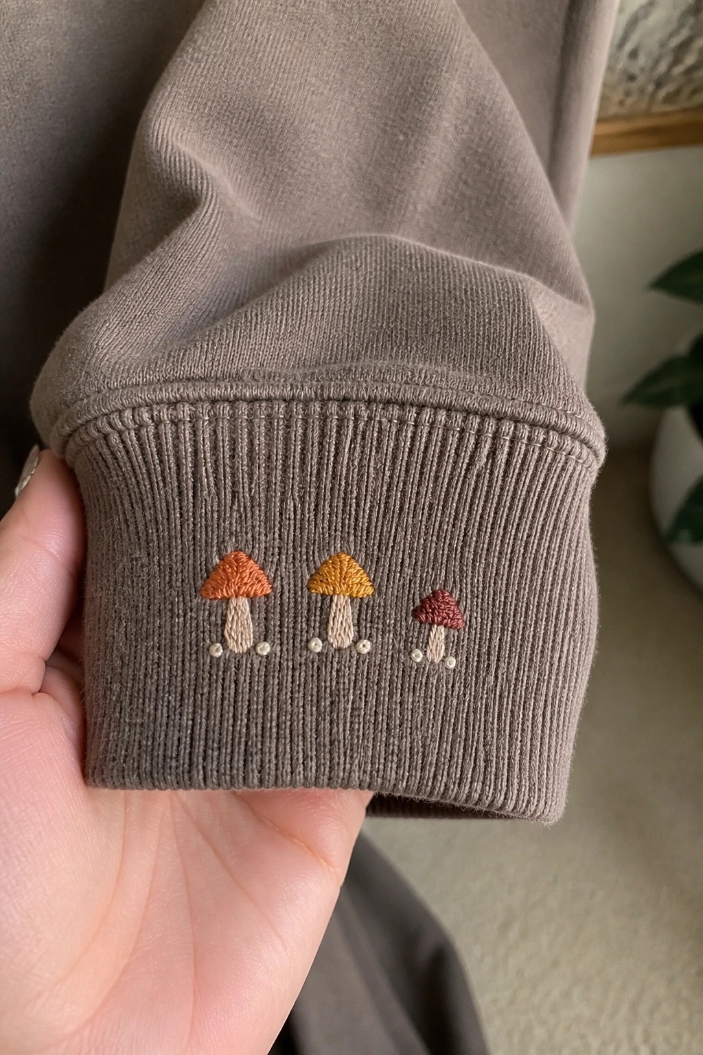 Gray ribbed cuff with three embroidered mushrooms in orange, yellow, and red.