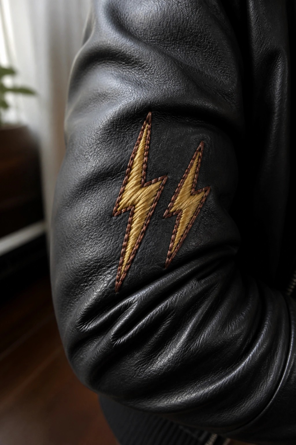Black leather jacket sleeve with two yellow lightning bolt embroideries and brown stitching.