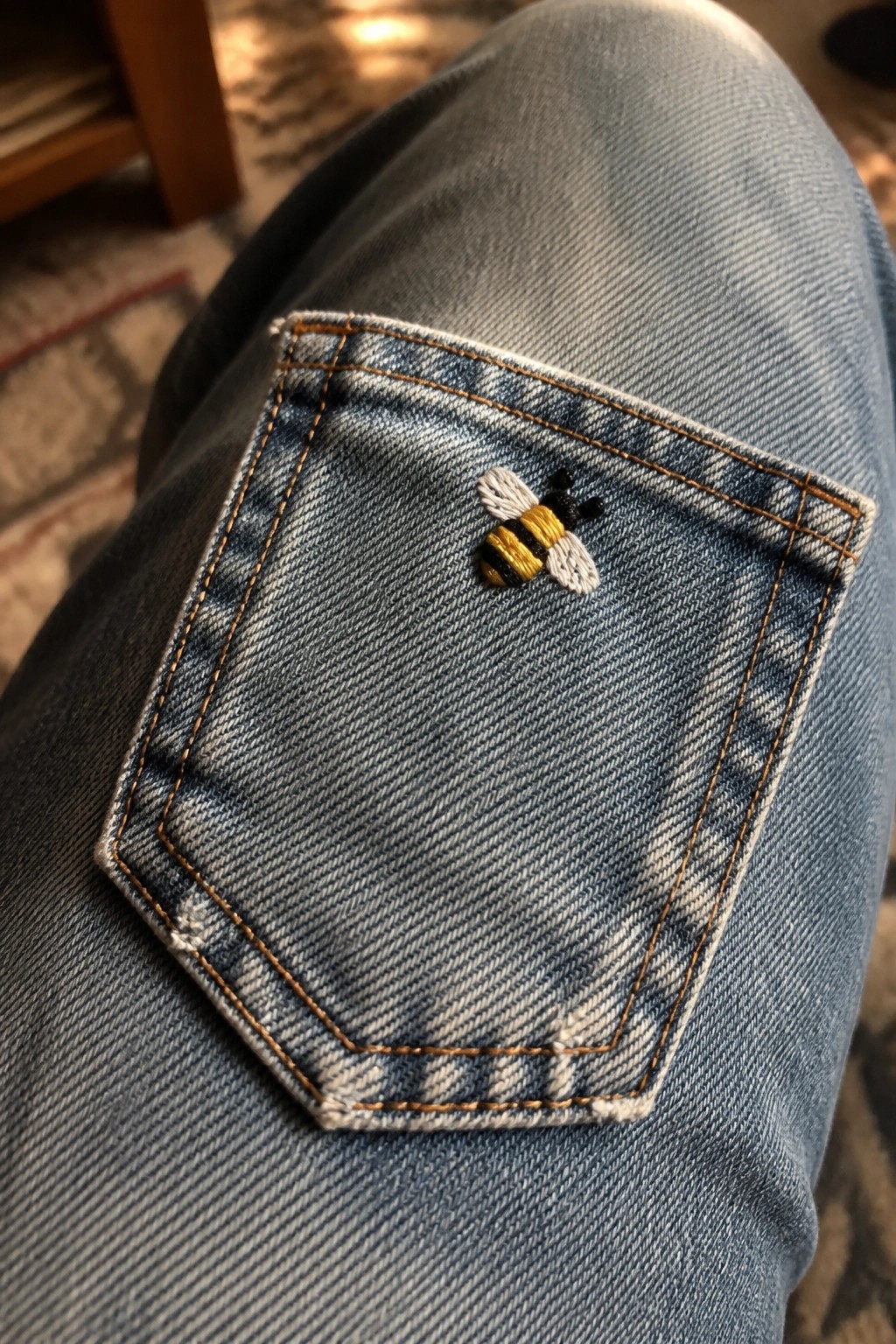 A small embroidered bee sits on the corner of a blue denim jeans pocket.