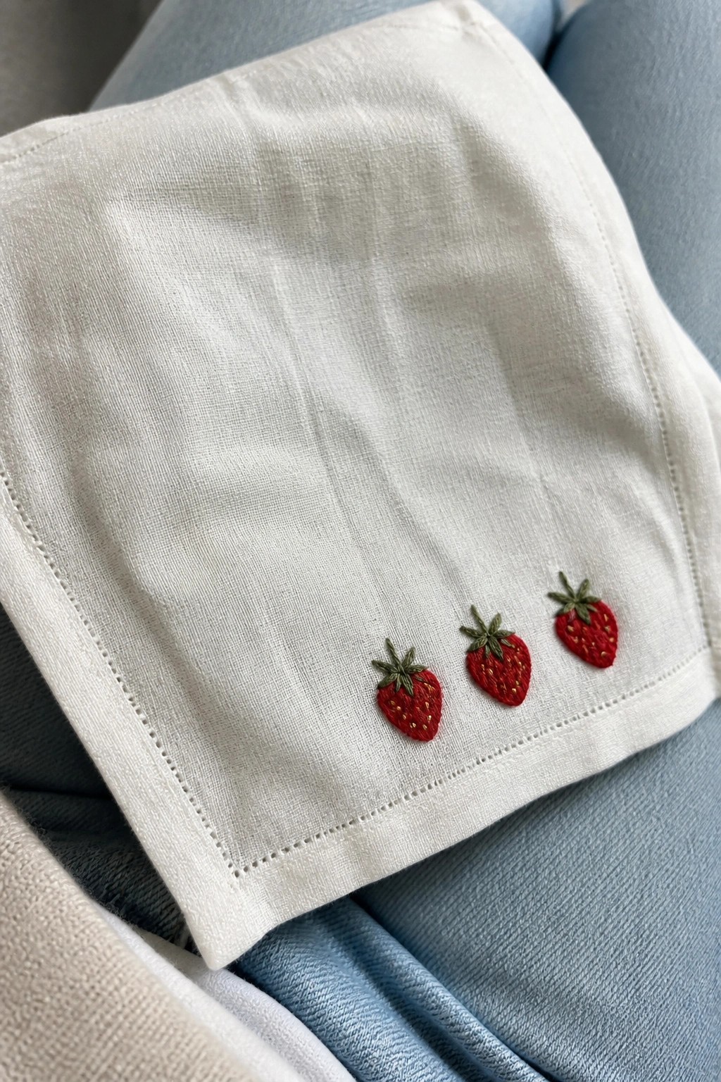 White fabric with three red strawberry embroideries on blue denim.