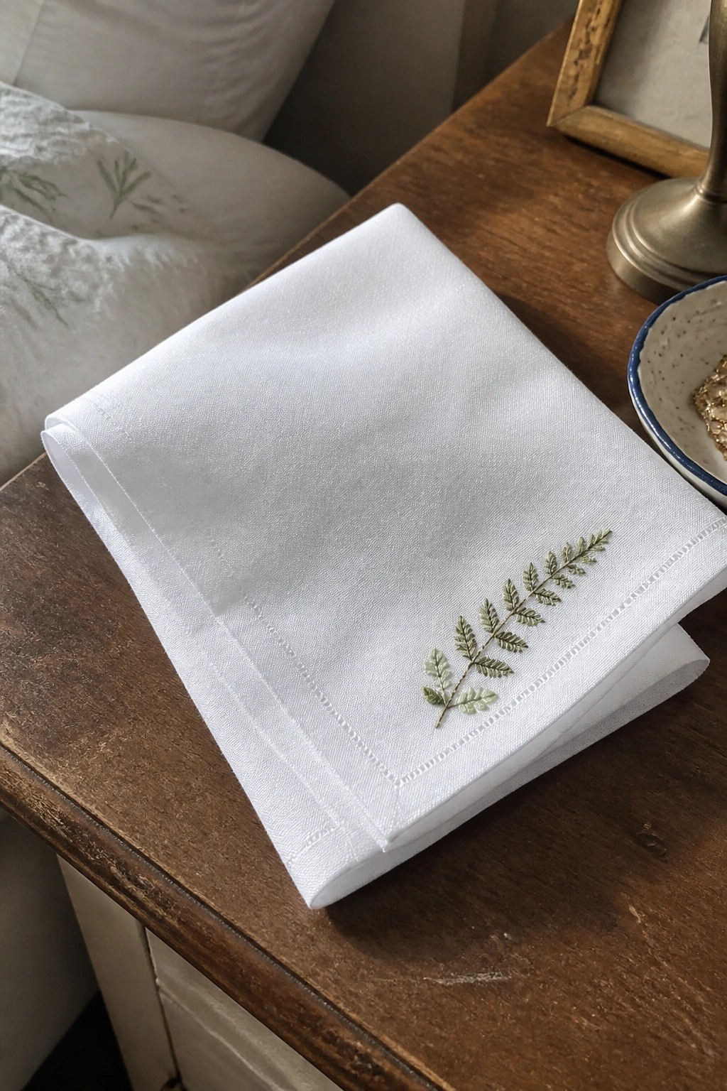 White folded napkin with green fern embroidery on wooden bedside table