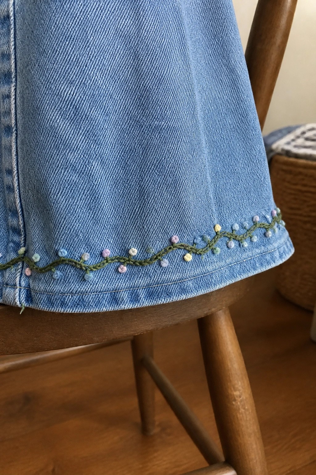 Blue denim garment with green vine and pastel dot embroidery on wooden chair.
