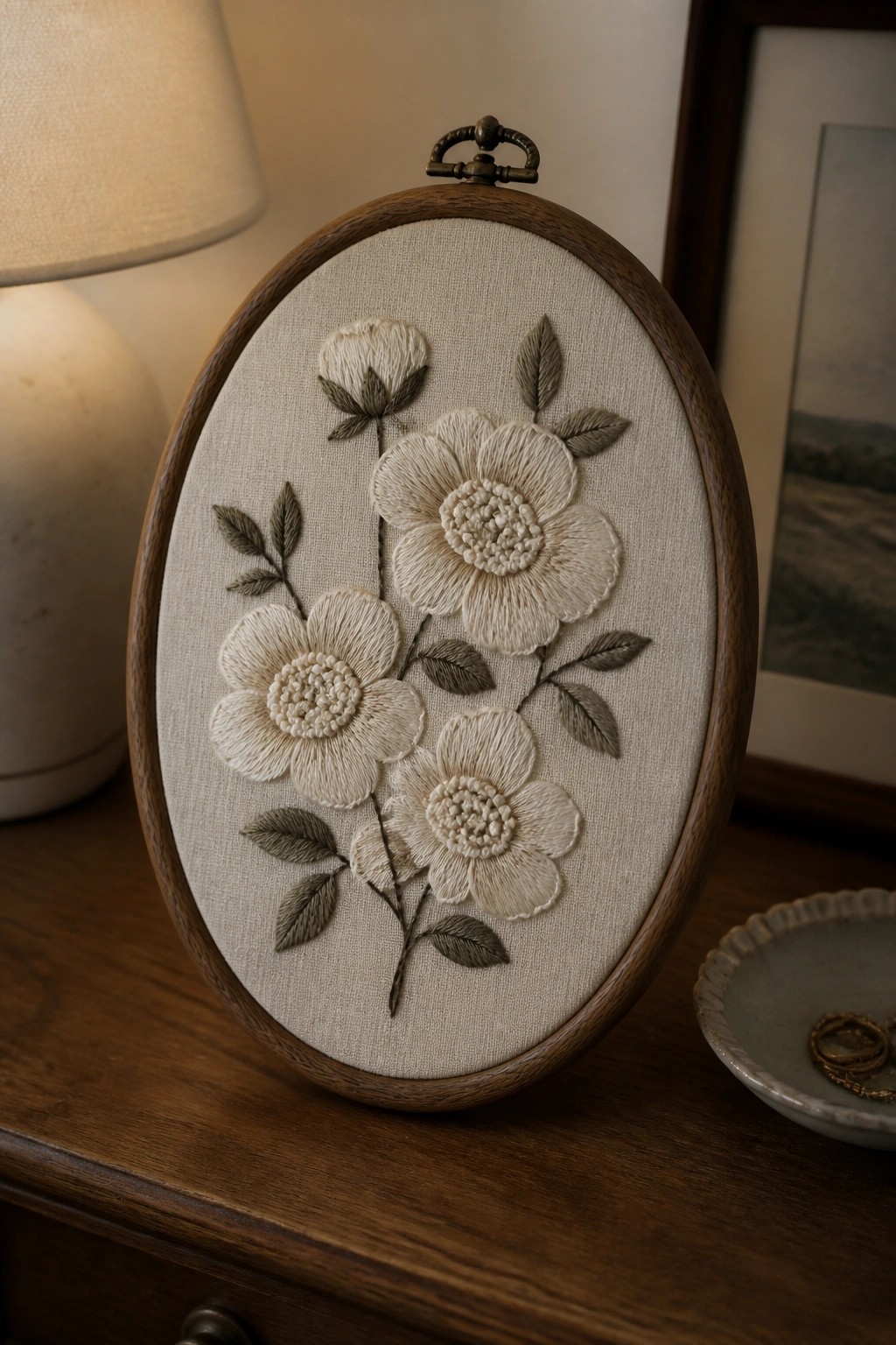 Oval wooden hoop with cream floral embroidery and green leaves on beige fabric