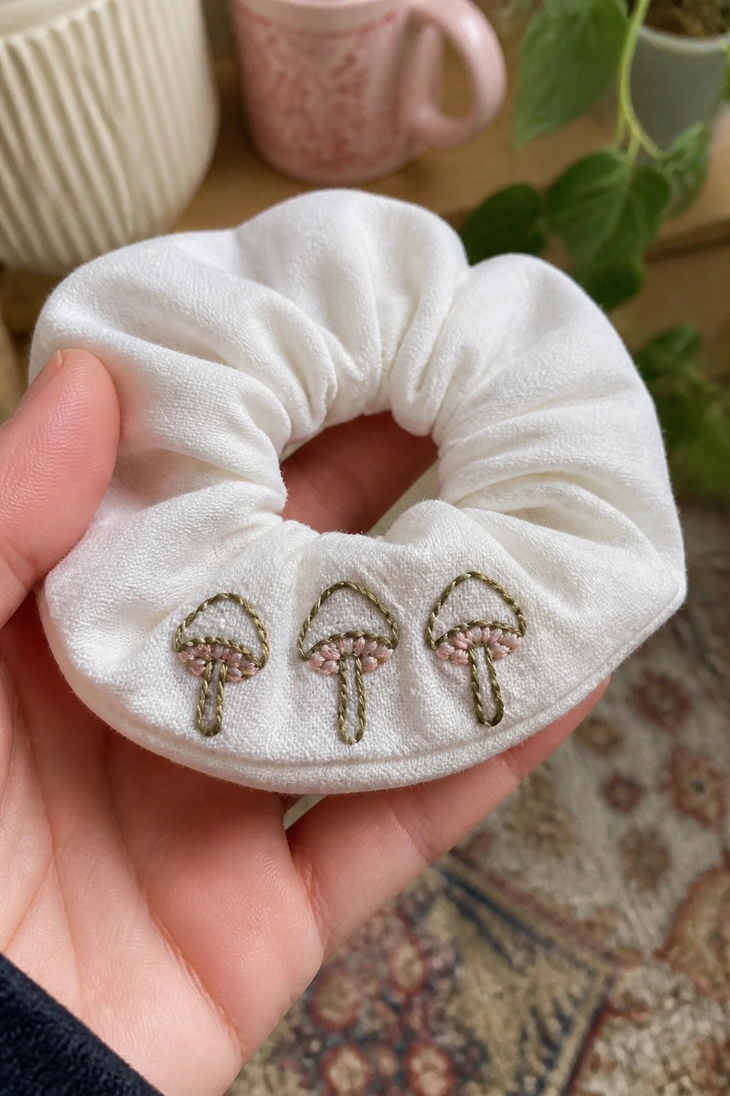 White scrunchie with three pink-and-green embroidered mushrooms held in hand