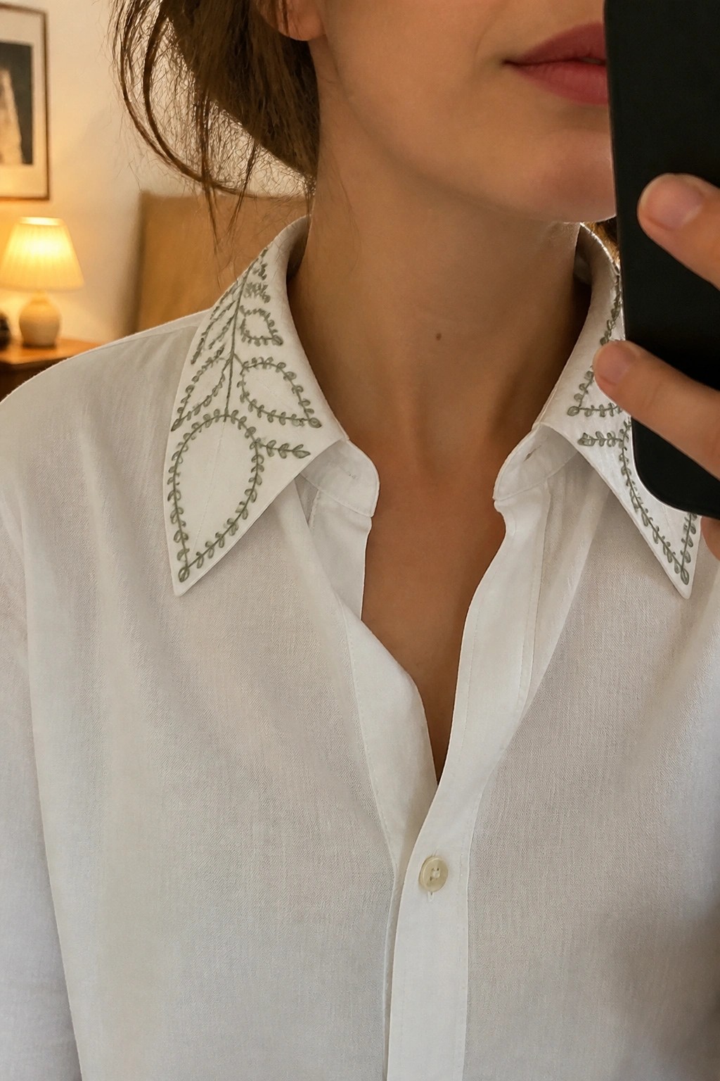 White shirt with green embroidered leaf patterns on pointed collar, hand holding phone.