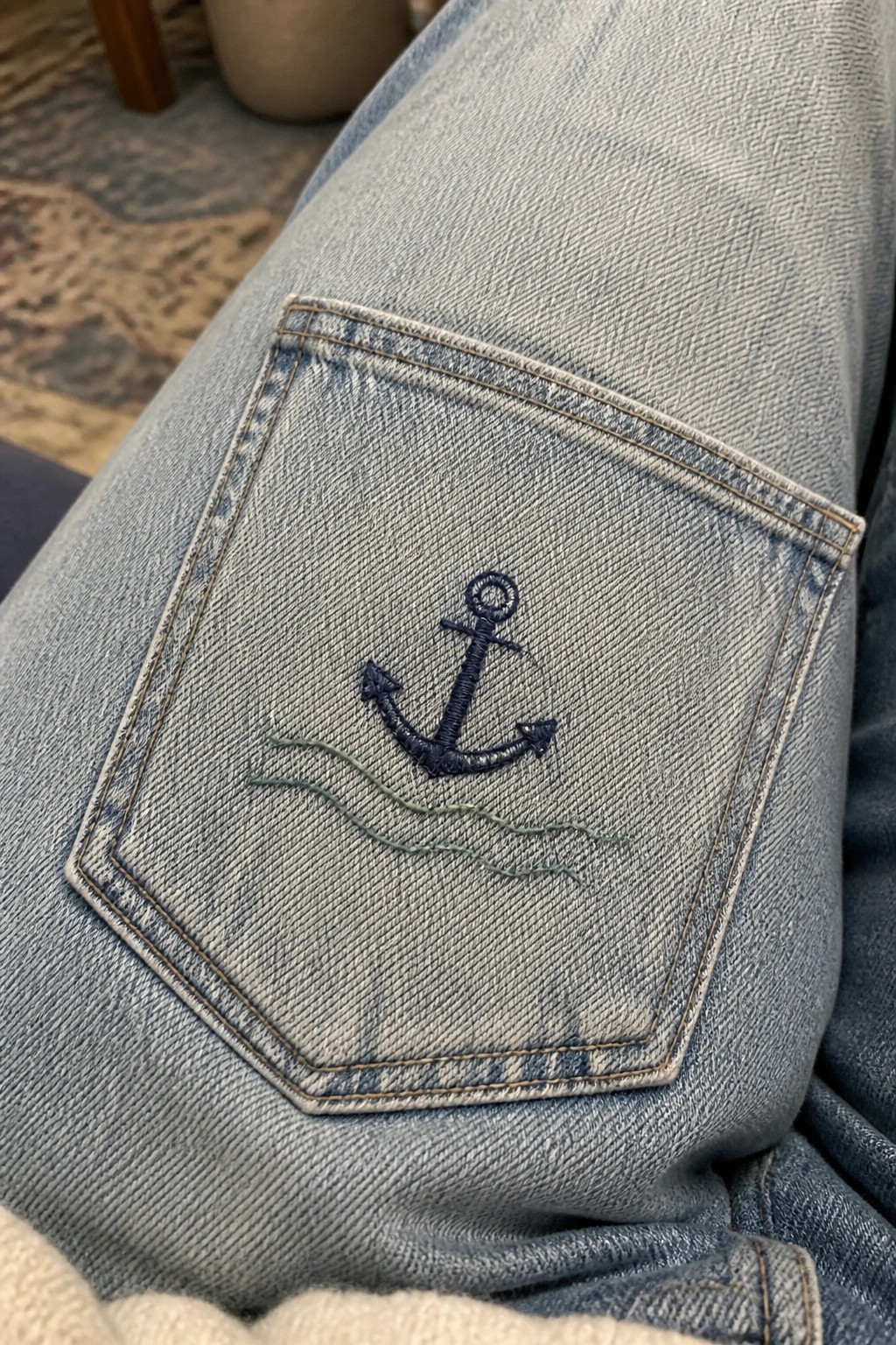 Denim jeans back pocket with navy embroidered anchor and green waves below.