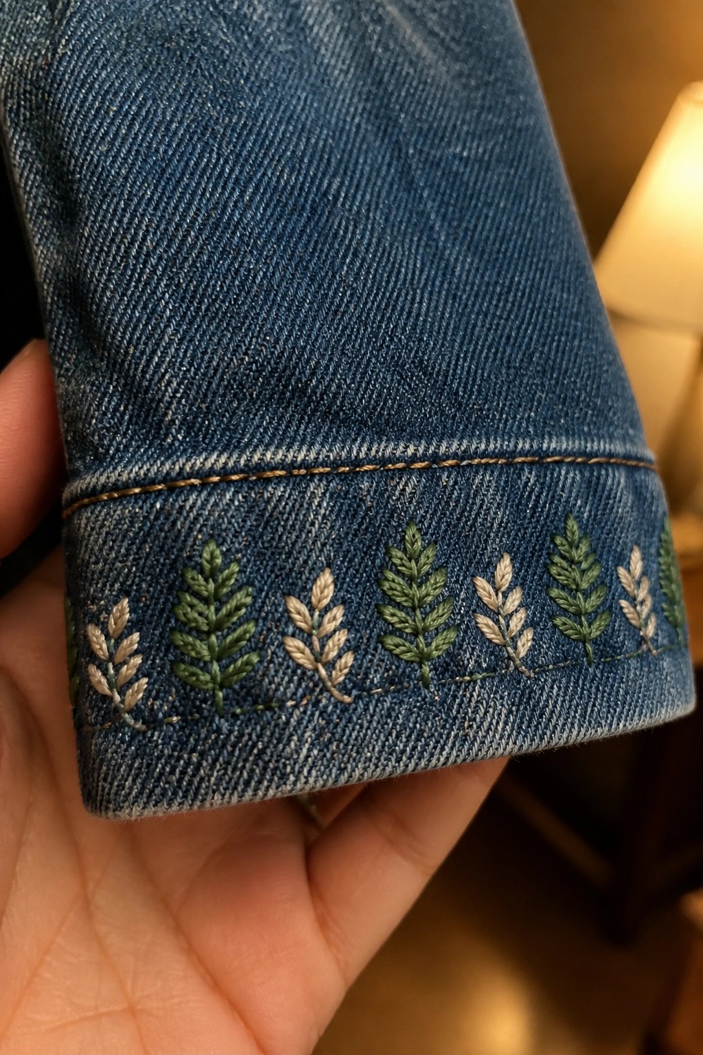 Blue denim cuff with green and beige embroidered fern patterns held by hand