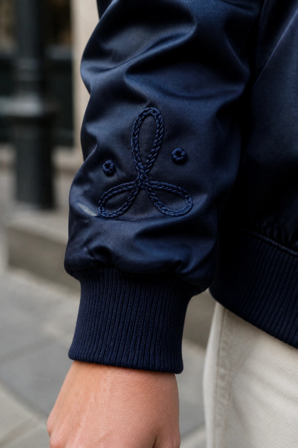 Navy bomber jacket sleeve with dark blue embroidered logo and ribbed cuff