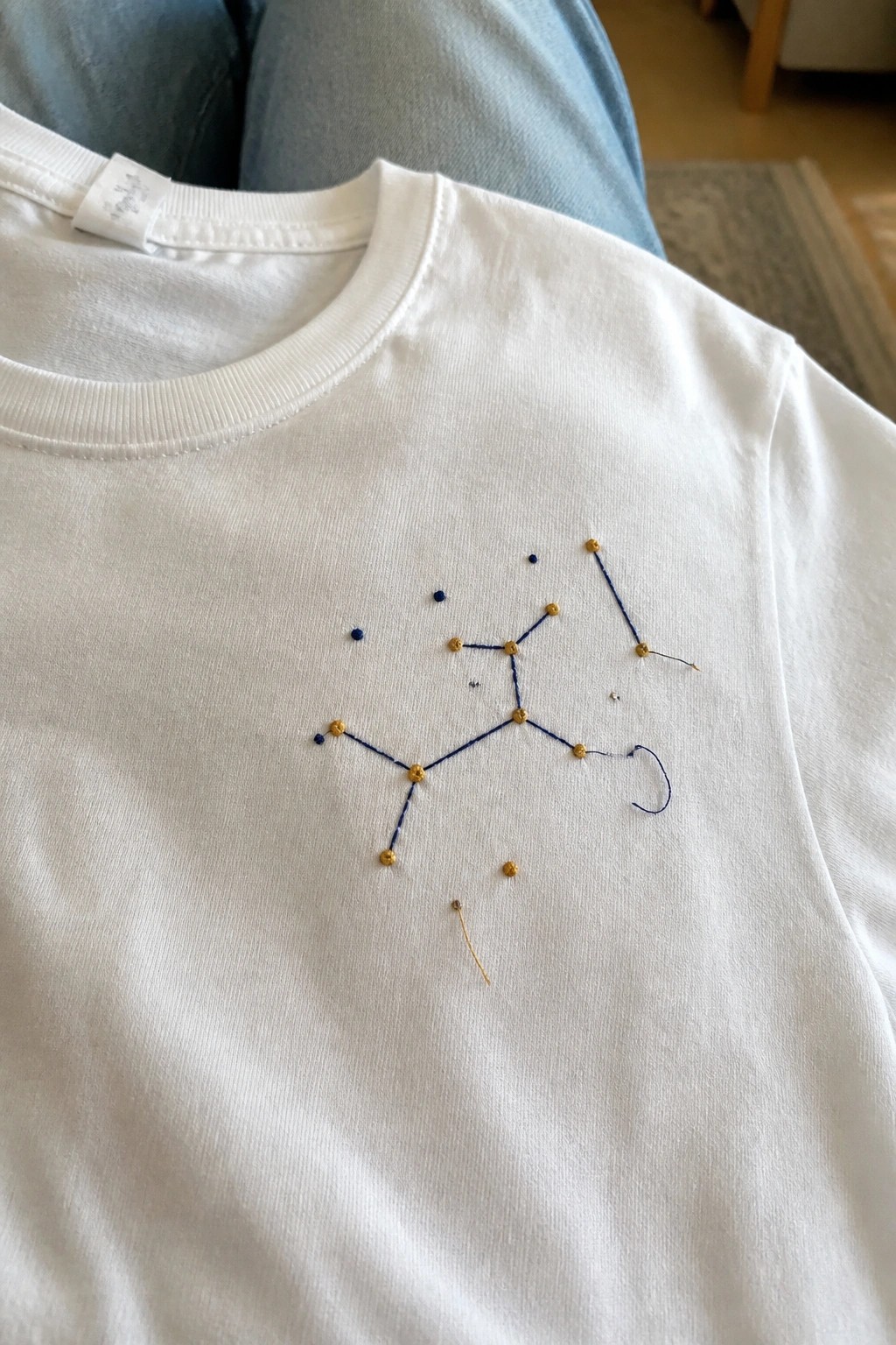 White t-shirt with blue embroidered constellation and scattered gold dots on chest