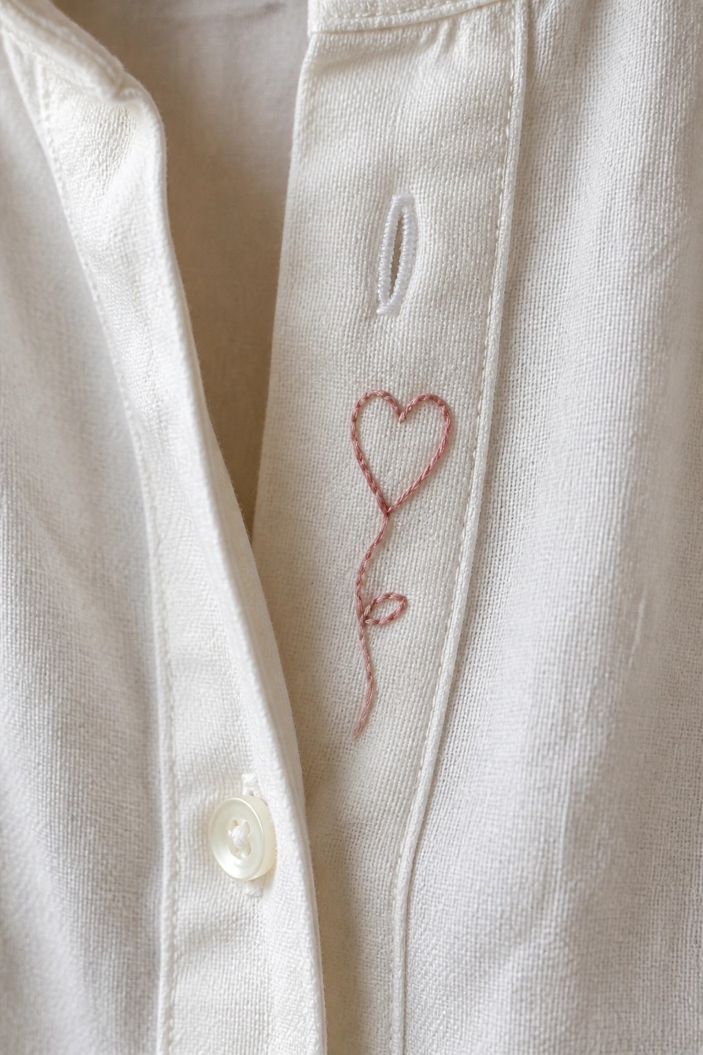 White linen shirt with pink embroidered heart balloon, button and buttonhole