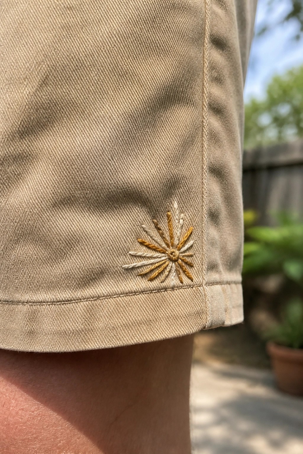 Close-up of a small yellow and white radiating embroidery design on the hem of beige shorts.
