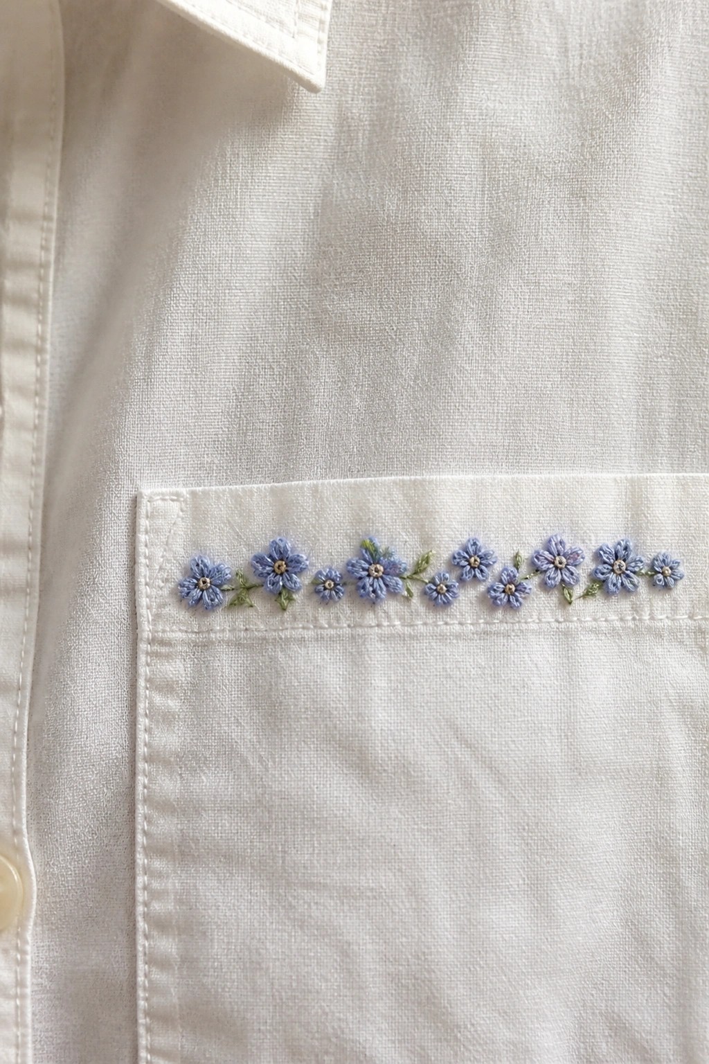 White shirt pocket with row of blue embroidered flowers and green leaves