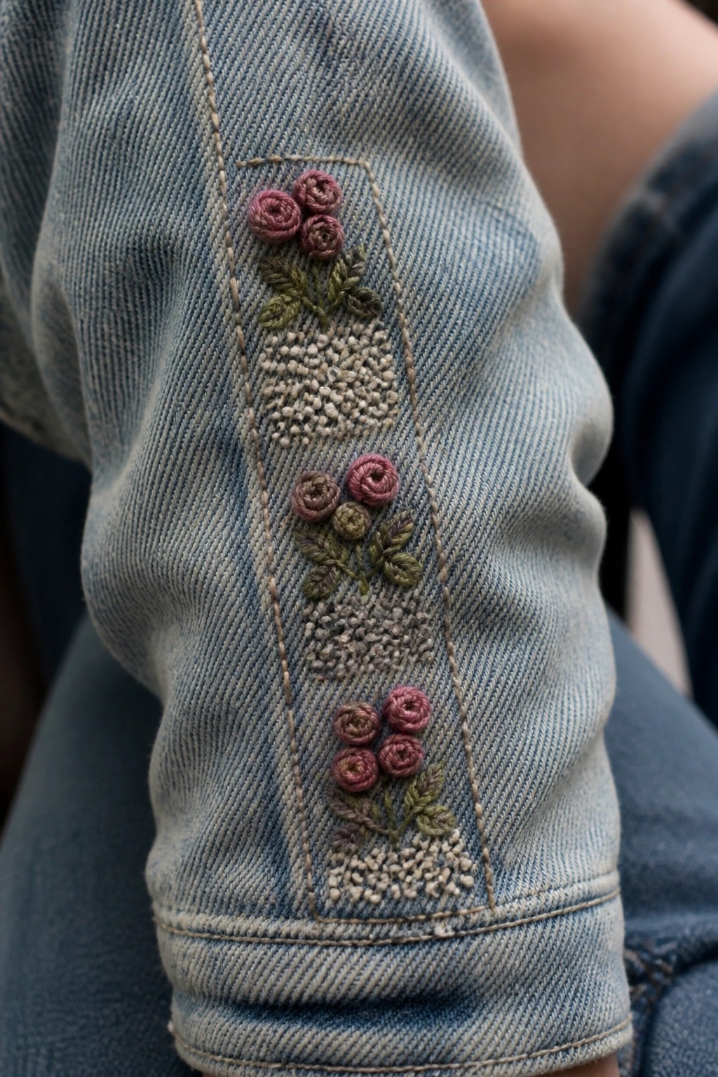 Blue denim sleeve embroidered with three pink rose bouquets and green leaves.