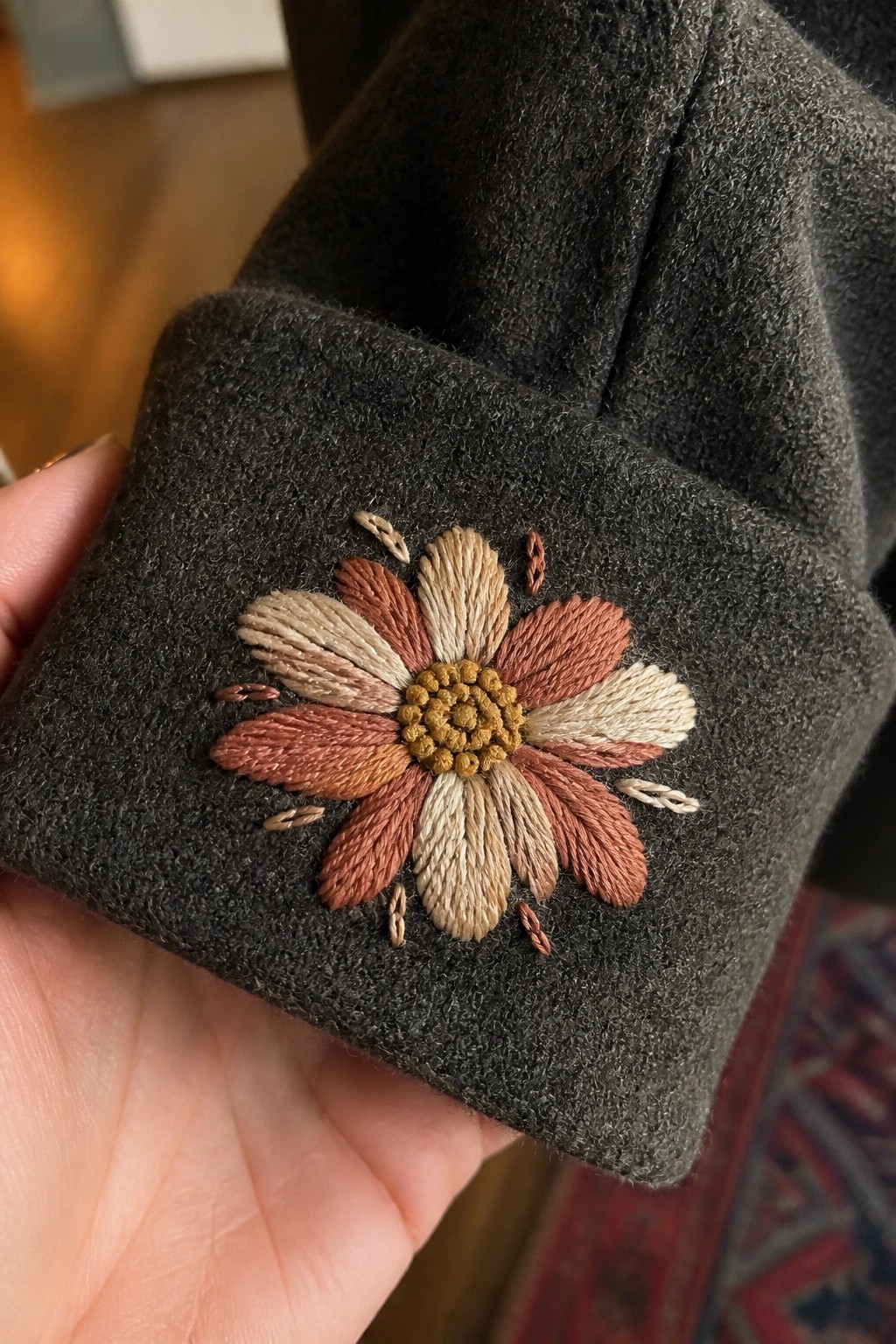 Hand holding dark gray wool cuff with embroidered brown and beige flower