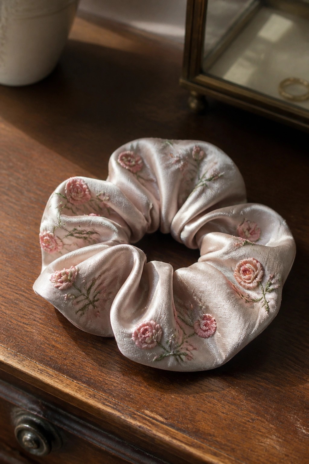 Light pink satin scrunchie with pink floral embroidery on wooden table