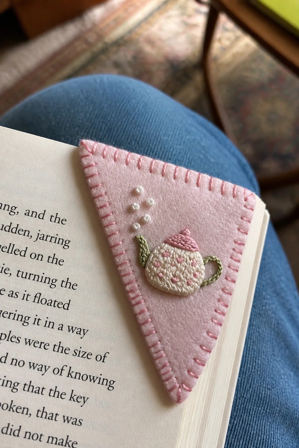 A pink triangular felt bookmark with an embroidered teapot sits in an open book.