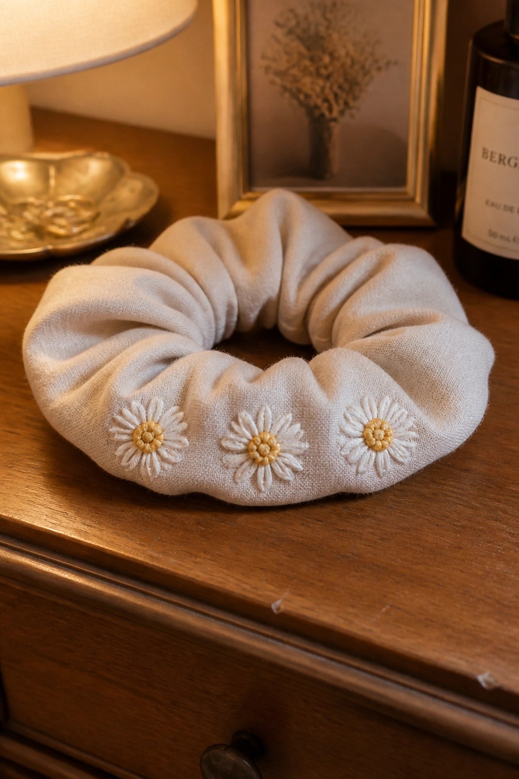 Off-white scrunchie with three daisy embroideries on wooden dresser surface