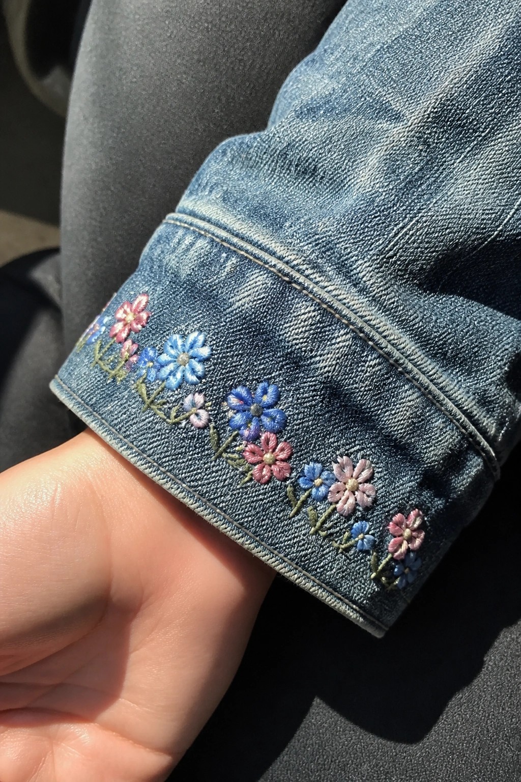 Blue denim jacket cuff embroidered with colorful pink and blue flowers on wrist.