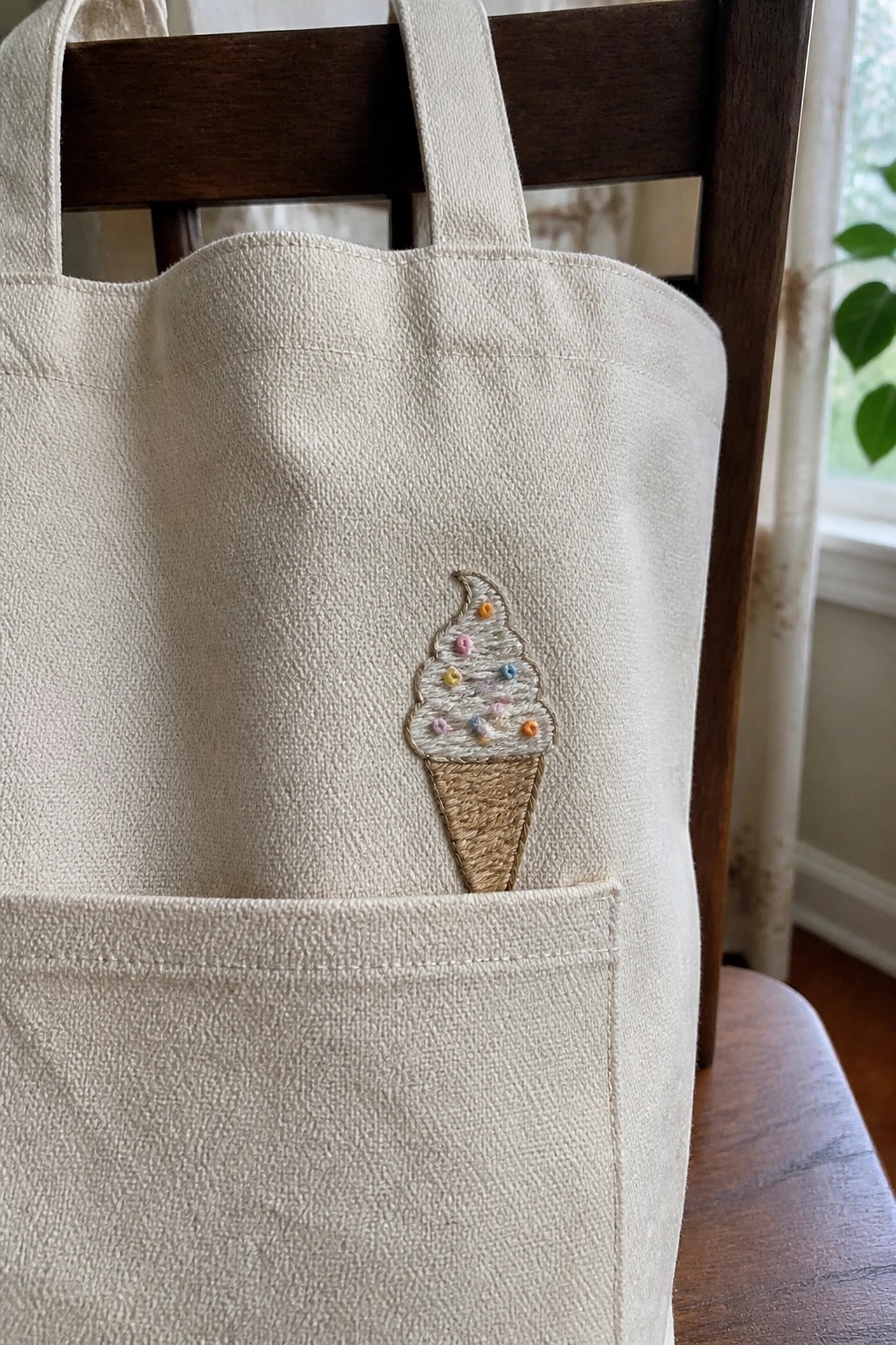 Cream canvas tote bag with embroidered ice cream cone and sprinkles on chair