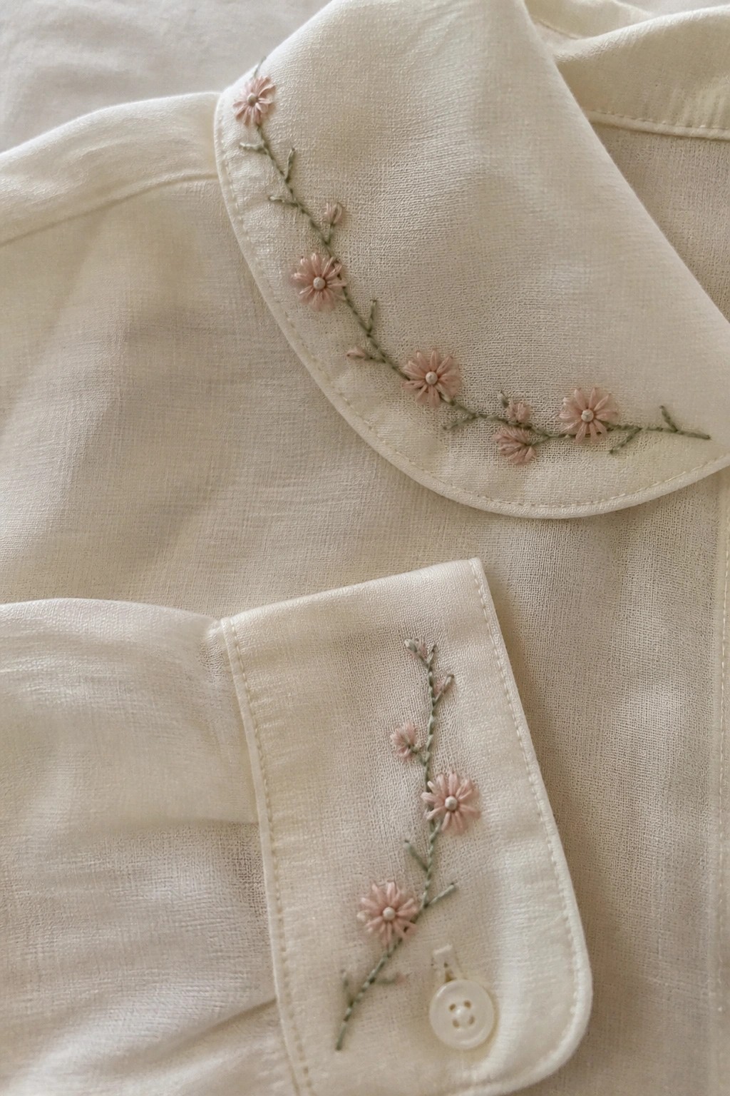 Close-up of cream shirt collar and cuff with pink flower vine embroidery along the edges.