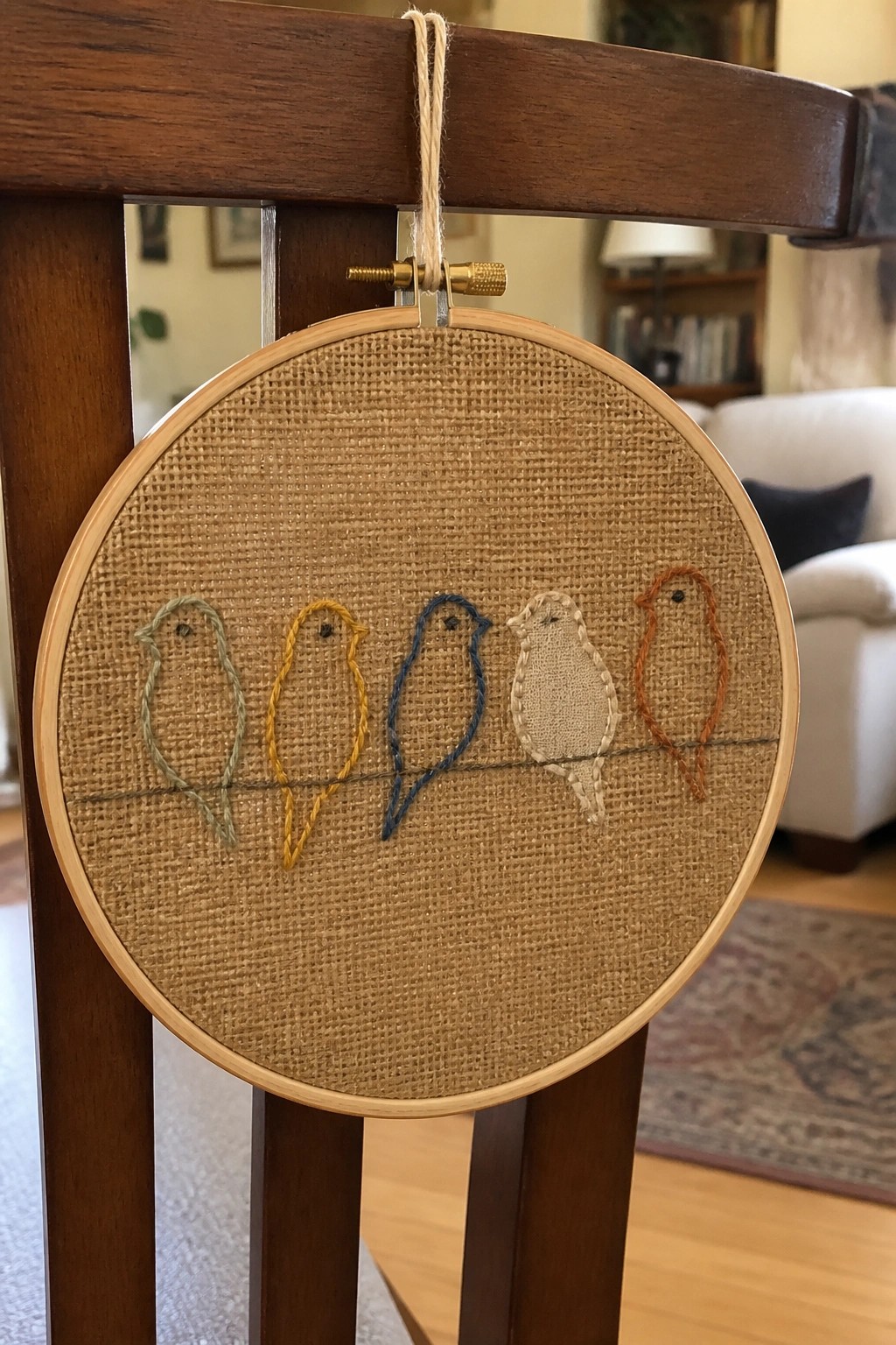 Wooden embroidery hoop with five colorful birds stitched on burlap, hanging from chair