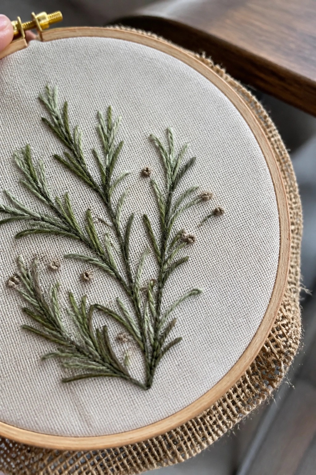 Wooden embroidery hoop with green stitched foliage branches on beige fabric