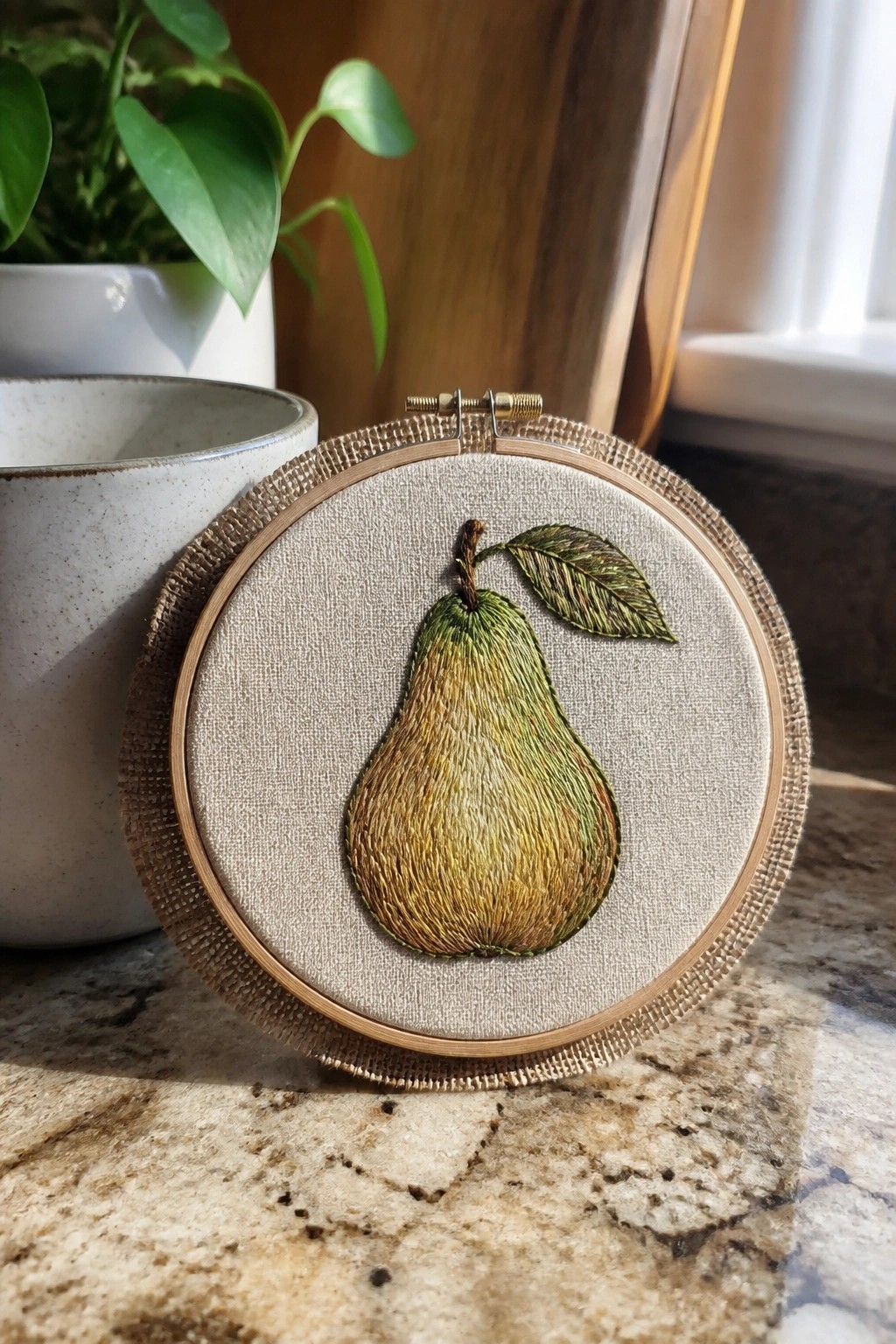 Embroidered green-yellow pear with leaf in wooden hoop on marble counter