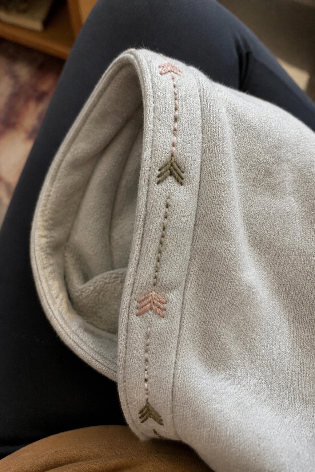 Light gray fabric cuff with a vertical row of small embroidered arrows in pink and green threads along the seam.