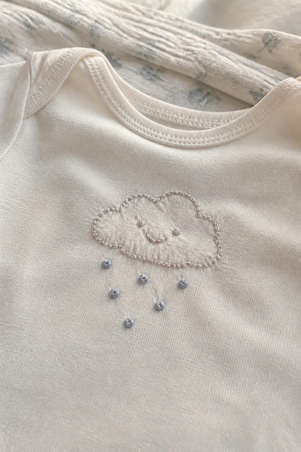 White onesie with embroidered smiling cloud and blue raindrops on chest