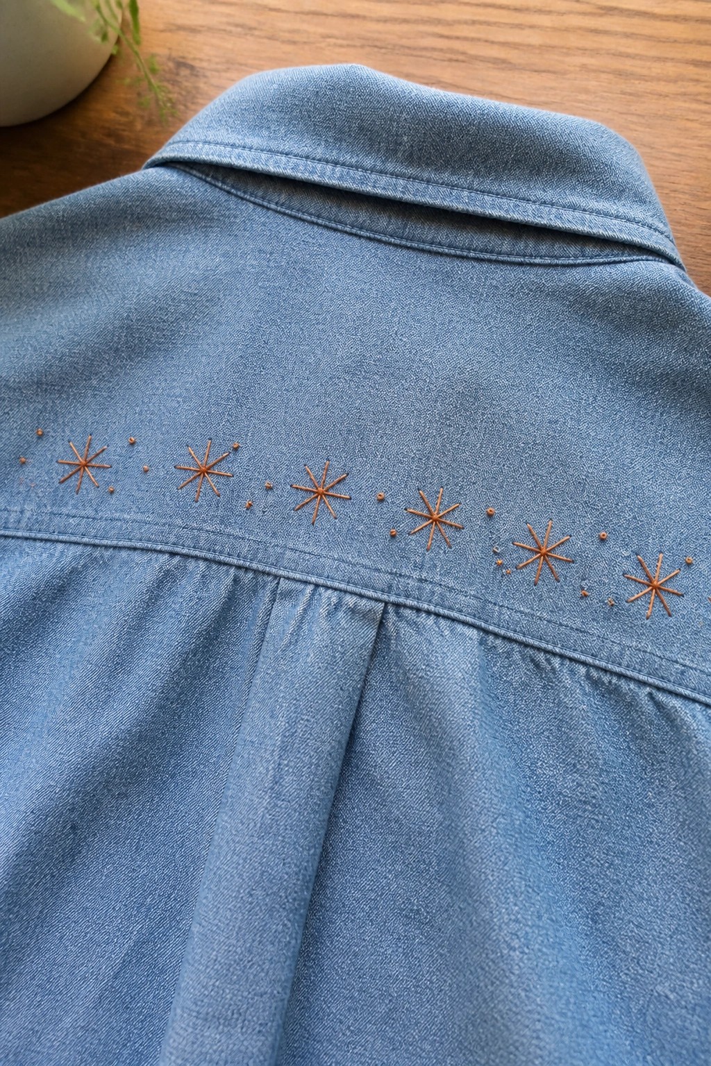 Blue denim shirt yoke with a horizontal row of small orange starburst embroidery and dots.