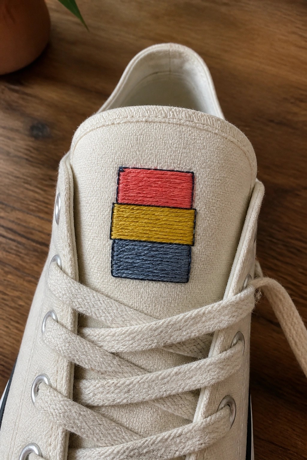 White canvas sneaker with red, yellow, and blue embroidered stripes on side