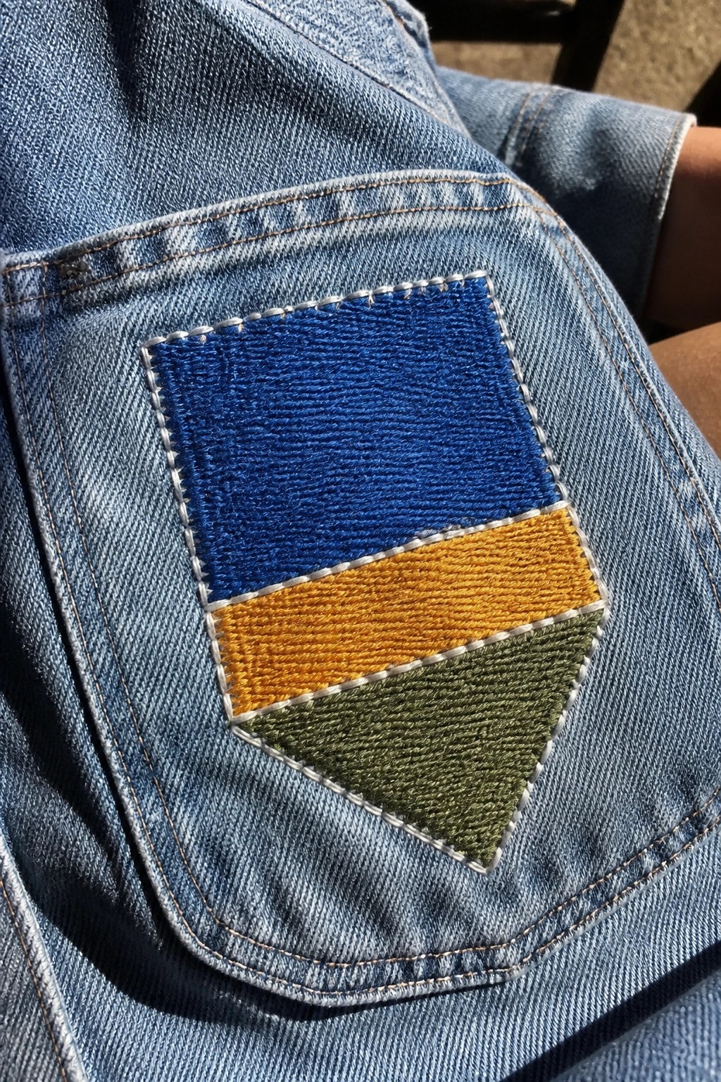 Blue denim pocket with shield-shaped blue, yellow, and green patch.