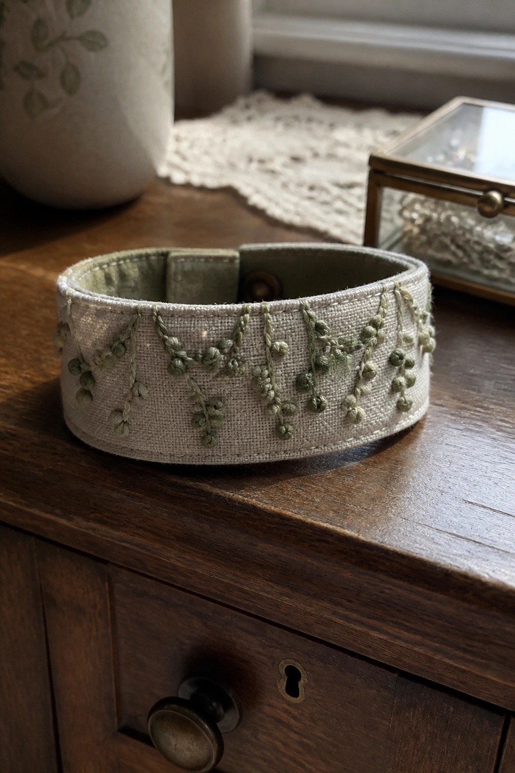 Beige embroidered fabric cuff with green vines on dark wooden furniture.