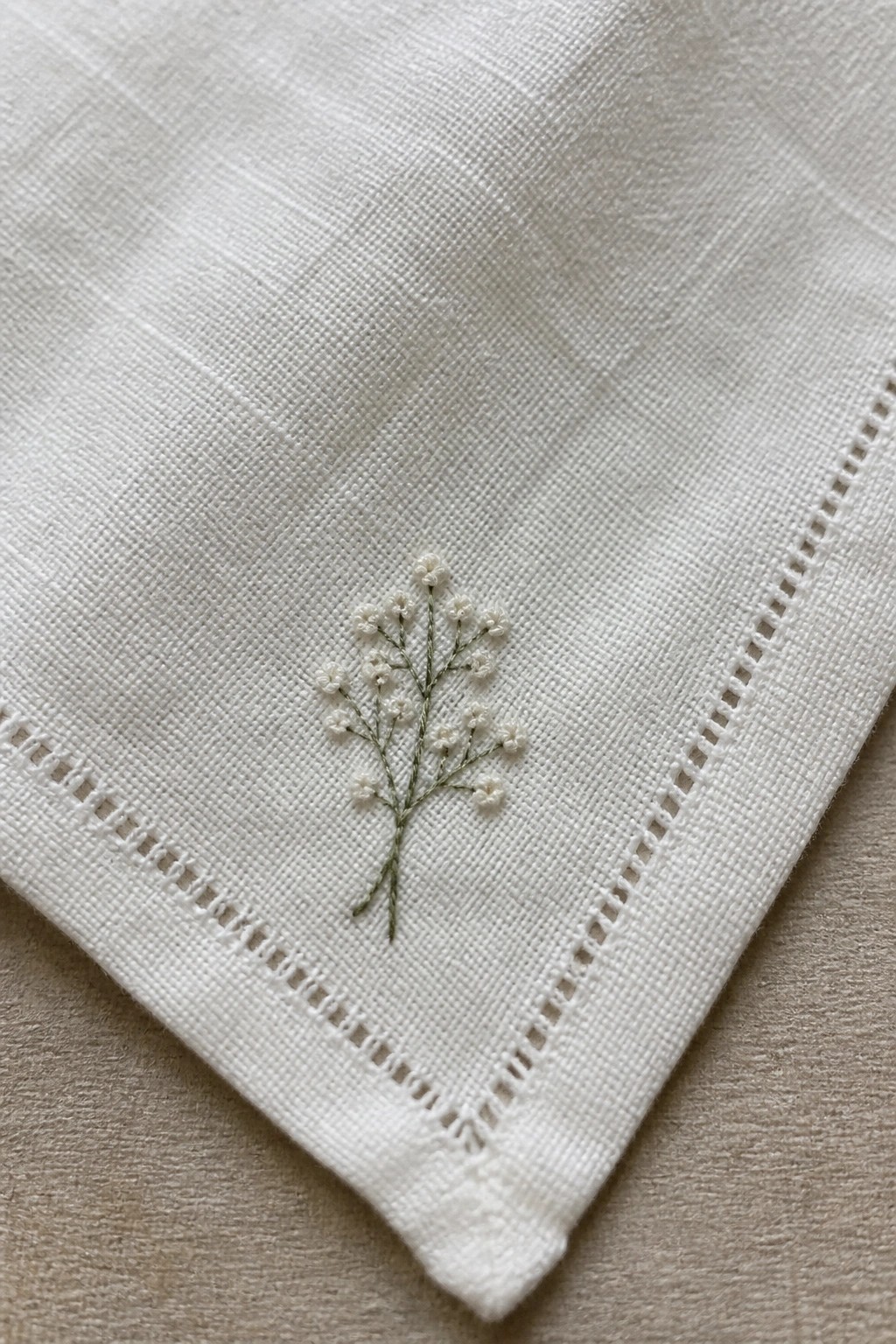 White linen fabric with embroidered white flowers on green stems and hemstitched border.