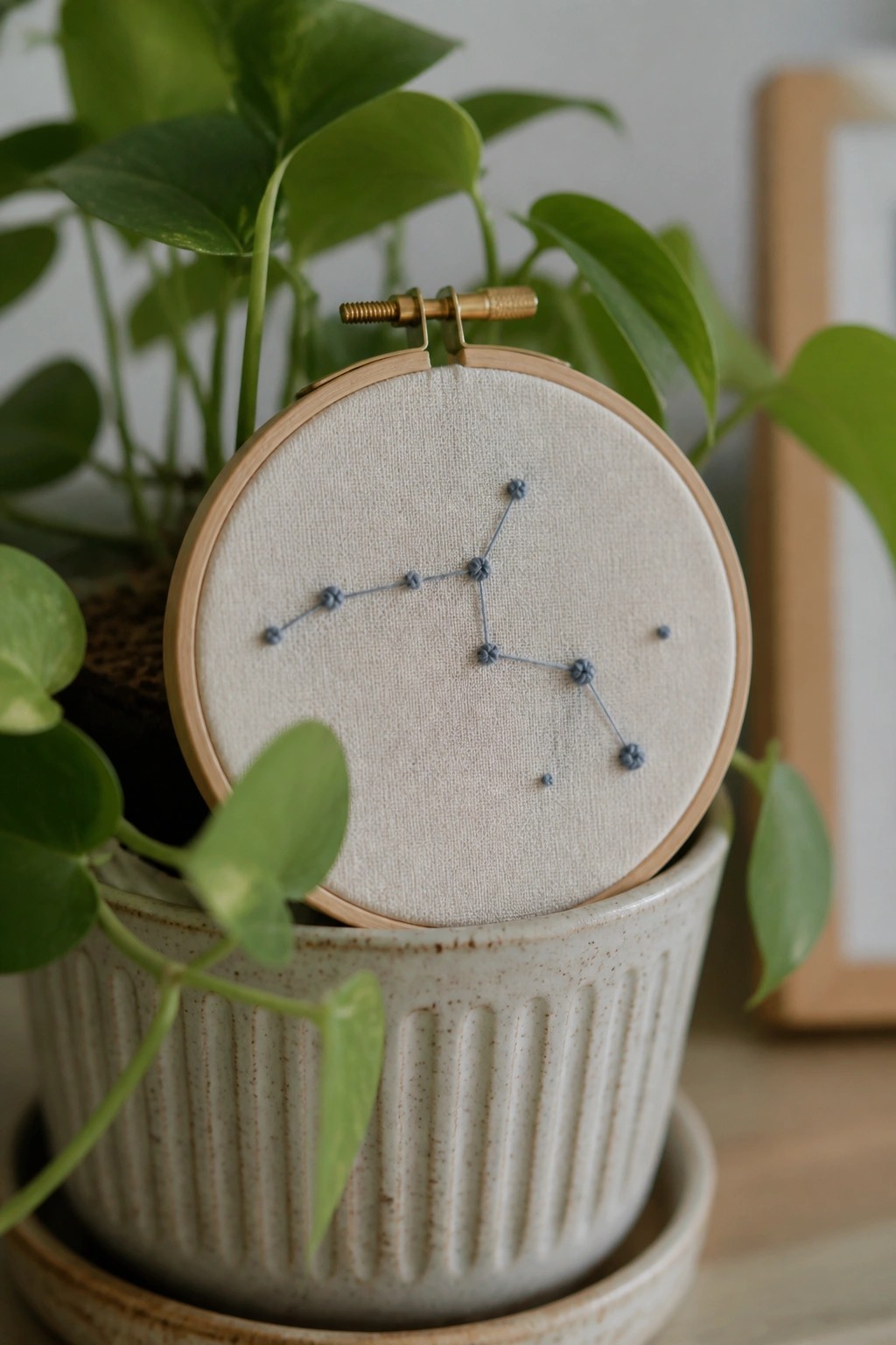 Wooden embroidery hoop with blue constellation stitches in a potted green plant.