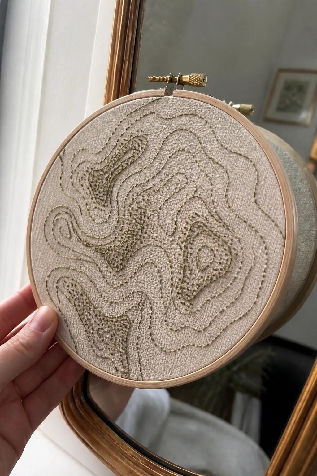 Hand holding wooden hoop with abstract wavy embroidery on beige fabric