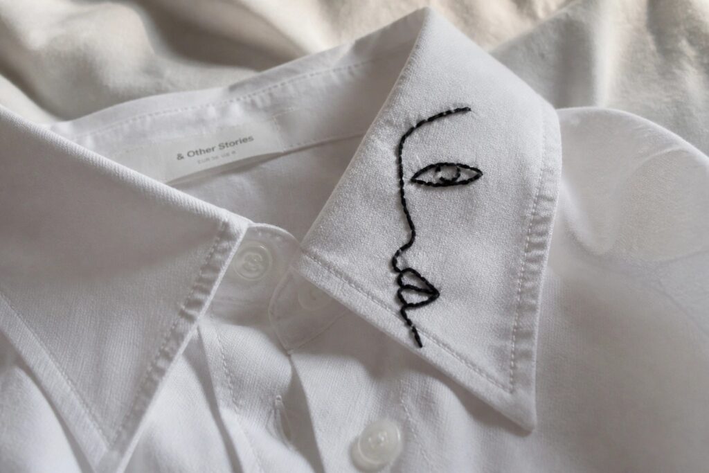 White shirt collar with black minimalist line embroidery of a face profile